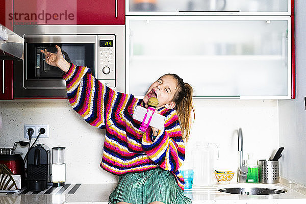 Mädchen spielt mit Mikrofon und Smartphone in der heimischen Küche