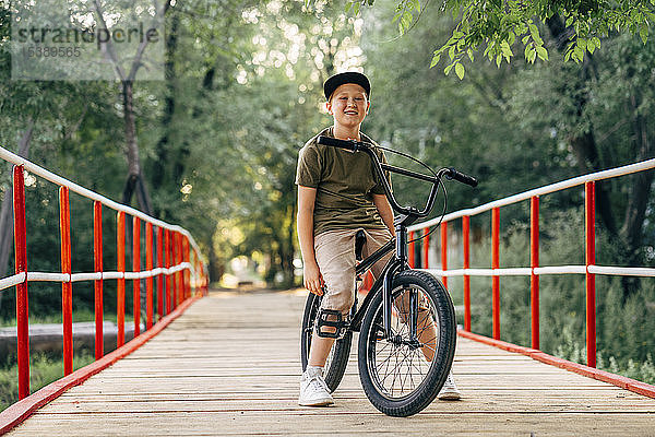 Porträt eines lächelnden Jungen mit bmx-Fahrrad auf der Brücke