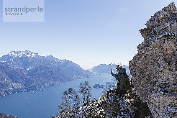 Italien  Como  Lecco  Frau auf Wanderung in den Bergen über dem Comer See  auf einem Felsen sitzend und die Aussicht geniessend