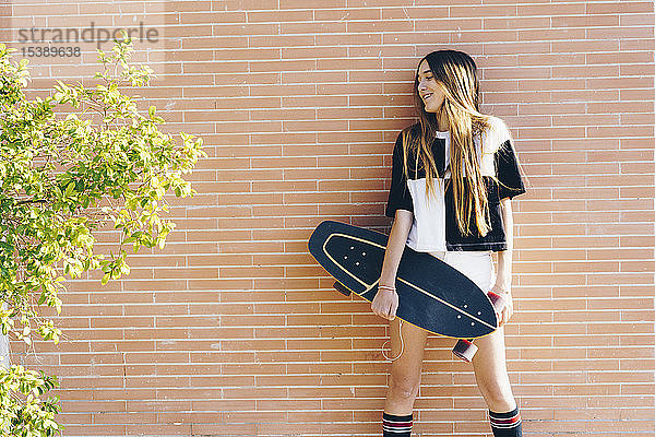 Spanien  Teenager hält Skateboard an einer Ziegelmauer