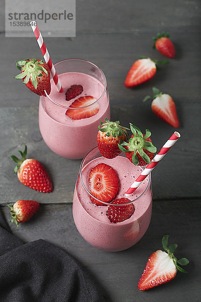 Gläser mit Erdbeer-Smoothie und Erdbeeren auf dunklem Holz