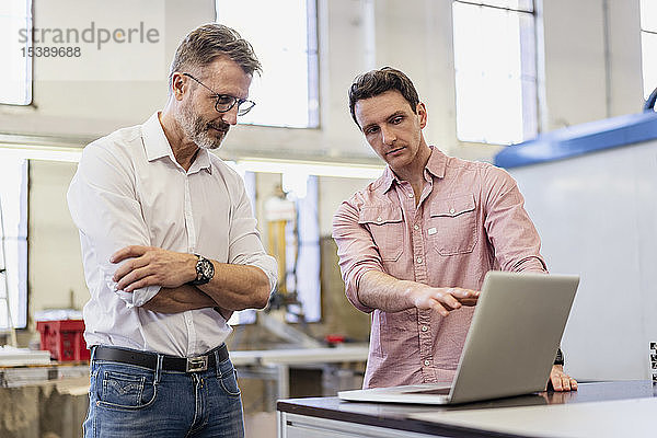 Zwei Kollegen in der Fabrik diskutieren am Laptop