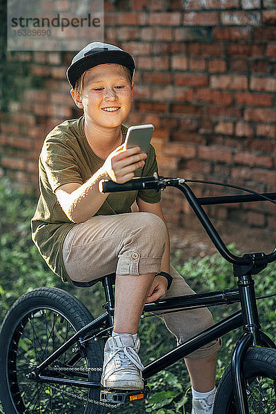Lächelnder Junge mit bmx-Fahrrad mit Handy