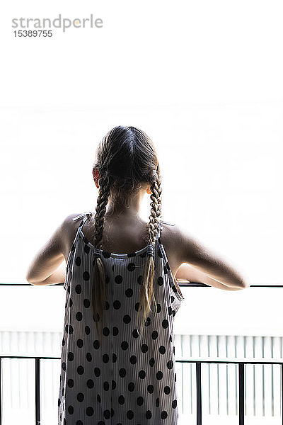 Rückansicht eines Mädchens in gepunktetem Kleid  das vom Balkon aus blickt