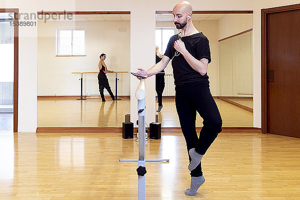 Balletttänzer beim Dehnen und Benutzen eines Mobiltelefons im Ballettstudio