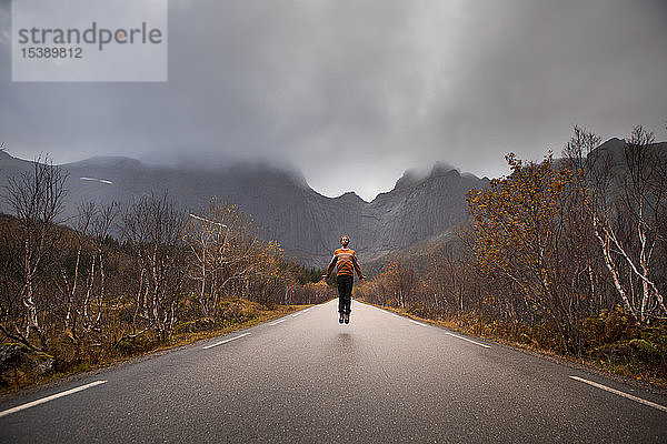 Norwegen  Lofoten-Inseln  Mann springt auf leere Straße  umgeben von einer Felswand