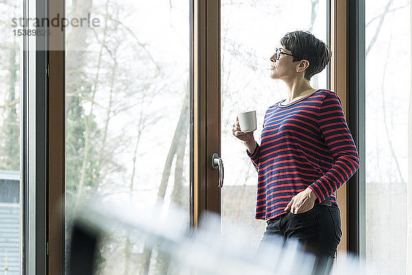 Frau mit Kaffeetasse  die aus der Terrassentür schaut