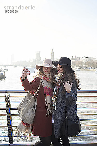 UK  London  zwei Frauen  die sich auf der Millennium-Brücke mit dem Stadtbild im Hintergrund ein Selfie leisten