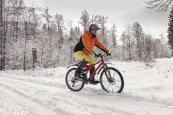 Mann fährt Mountainbike auf Weg im Winterwald