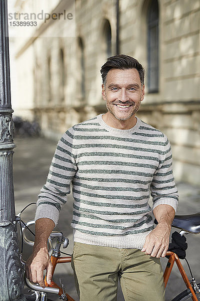 Porträt eines lächelnden Mannes mit Fahrrad in der Stadt