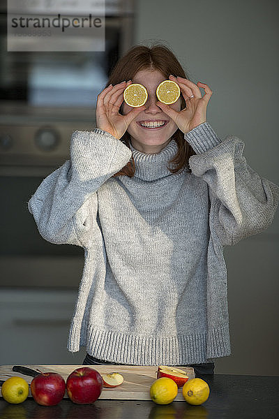 Lachendes Teenager-Mädchen hält Zitronenhälften vor ihren Augen