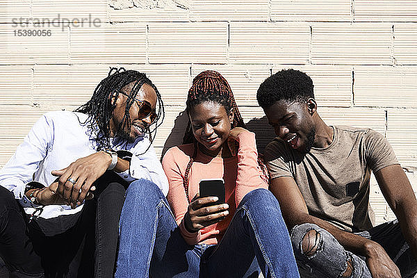Drei Freunde sitzen zusammen und schauen sich im Freien ein Video auf einem Smartphone an