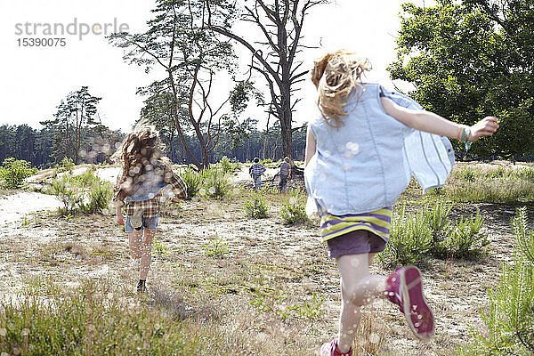 Rückansicht von zwei Mädchen  die durch eine Dünenlandschaft laufen