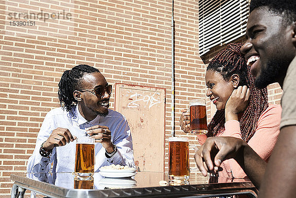 Drei glückliche Freunde trinken Bier in einer Bar im Freien