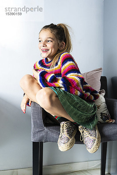 Glückliches Mädchen in gestreiftem Pullover sitzt zu Hause auf einem Stuhl