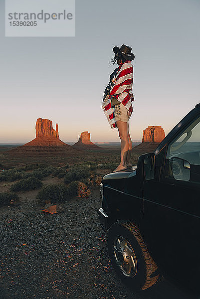 USA  Utah  Monument Valley  Frau mit der Flagge der Vereinigten Staaten von Amerika genießt den Sonnenuntergang im Monument Valley