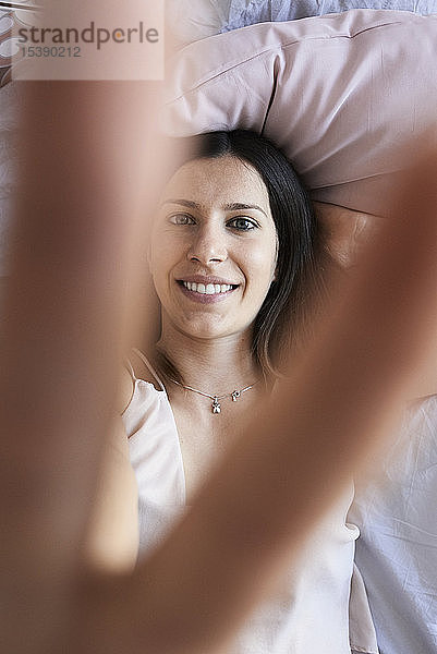 Porträt einer lächelnden  auf dem Bett liegenden jungen Frau mit Siegeszeichen  Draufsicht