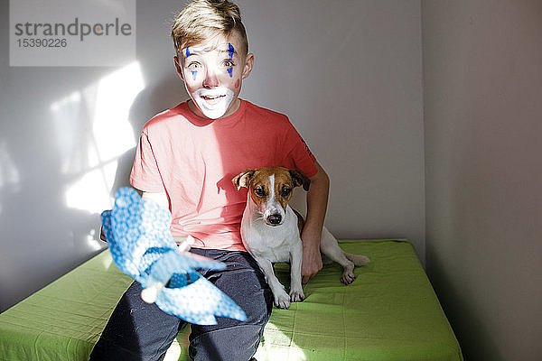 Portrait eines erstaunten  als Clown geschminkten Jungen mit Hund und Stecknadelrad zu Hause