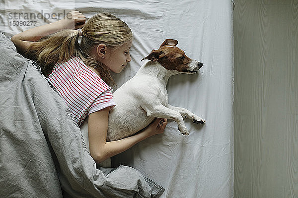 Blondes Mädchen im Bett liegend  ihr Hund schläft  Draufsicht