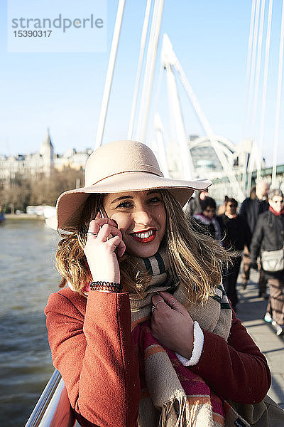 UK  London  stilvolle junge Frau  die auf der Millennium Bridge mit dem Handy telefoniert