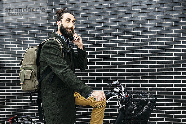 Mann mit E-Bike telefoniert mit dem Handy an einer Ziegelmauer