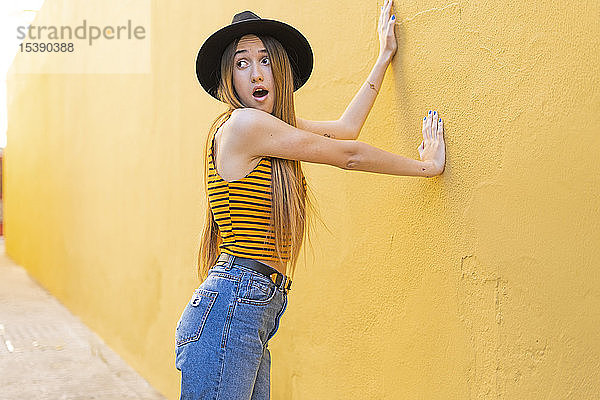 Porträt eines überraschten Teenager-Mädchens mit Hut an gelber Wand
