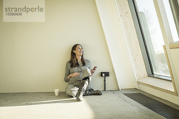 Schwangere Frau trinkt Tee und sitzt auf dem Boden ihres neuen Hauses