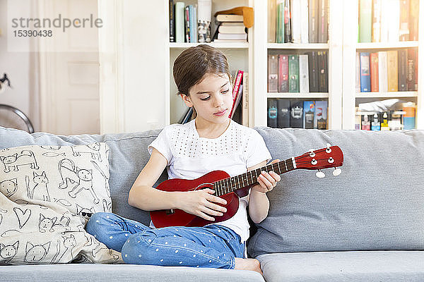 Porträt eines Mädchens  das zu Hause auf dem Sofa sitzt und Ukulele spielt
