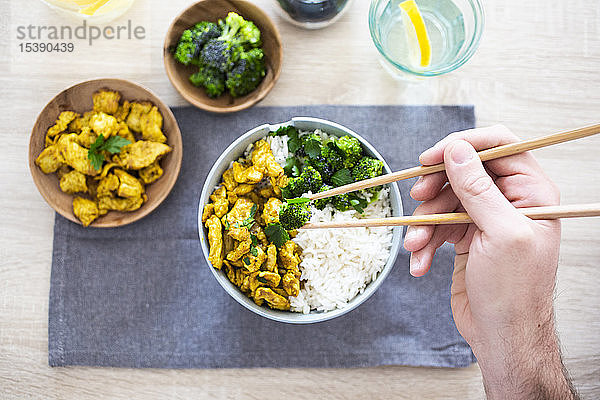 Curry-Huhn  Brokkoli und Reis  Mann hält Essstäbchen mit Brokkoli