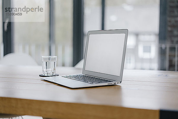 Laptop auf dem Schreibtisch im Büro mit einem Glas Wasser