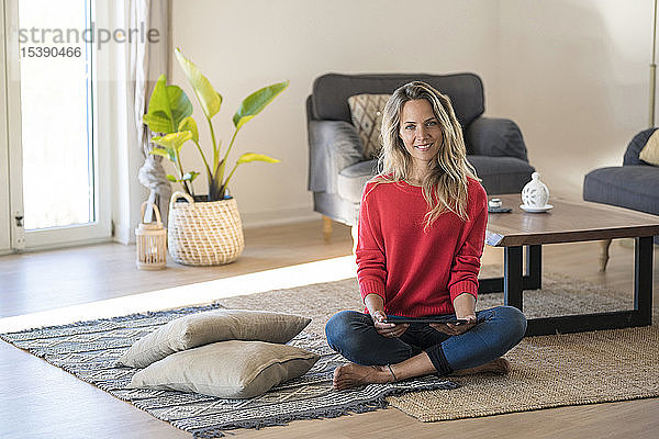 Porträt einer lächelnden Frau  die zu Hause auf dem Boden sitzt und ein Tablett hält