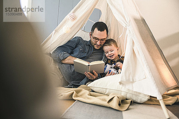 Vater und Sohn lesen zu Hause im Zelt gemeinsam ein Buch