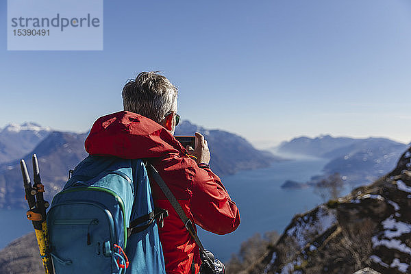 Italien  Como  Mann auf einer Wanderung in den Bergen über dem Comer See beim Fotografieren mit dem Handy