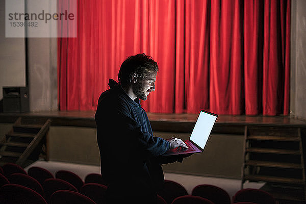 Regisseur steht mit Laptop im Theatersaal