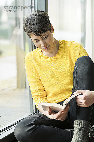 Frau sitzt auf dem Boden neben Terrassentür und liest Buch