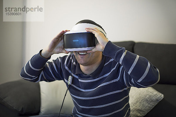 Lachender junger Mann zu Hause auf der Couch mit VR-Brille