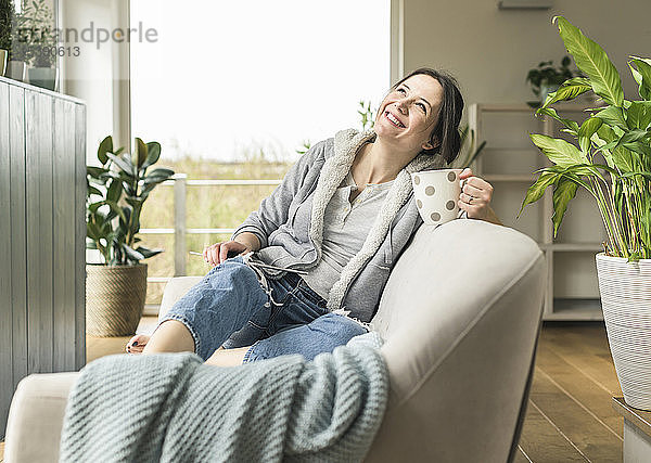 Glückliche Frau mit Becher und Tablette  die zu Hause auf der Couch sitzt