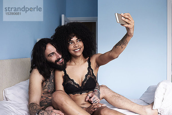 Glückliches  anhängliches junges Paar  das sich im Bett ein Selfie gönnt