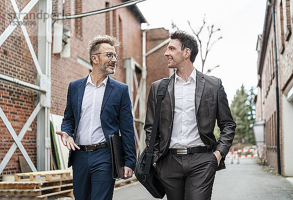 Zwei lächelnde Geschäftsleute gehen und unterhalten sich an einem alten Backsteingebäude