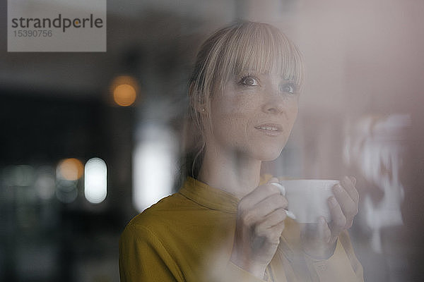 Bildnis einer schönen blonden Frau  die am Fenster steht und Kaffee trinkt