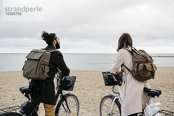 Paar mit E-Bikes am Strand mit Blick auf das Meer