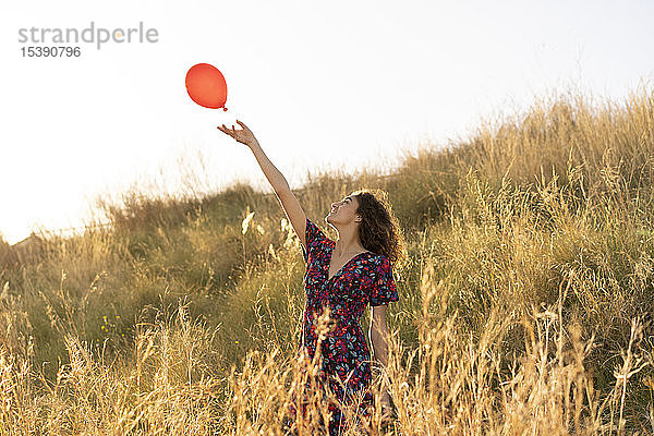 Glückliche junge Frau steht auf einer Sommerwiese und lässt einen roten Luftballon los