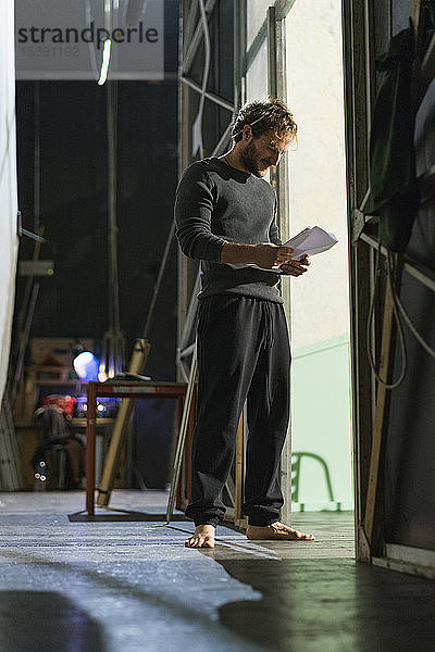 Barfüssiger Mann steht auf Theaterbühne und liest Skript