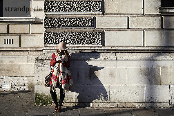 Stilvolle Frau  die mit ihrem Handy an einem Gebäude steht