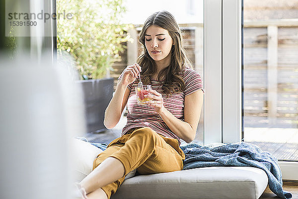 Junge Frau sitzt zu Hause am Fenster und isst einen Imbiss