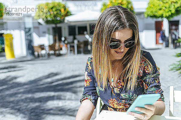 Spanien  Cádiz  Vejer de la Frontera  junge Frau sitzt im Straßencafé und schaut auf ihr Handy