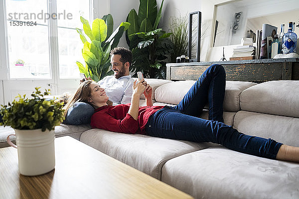 Auf dem Sofa liegendes Ehepaar mit Erben-Smartphones