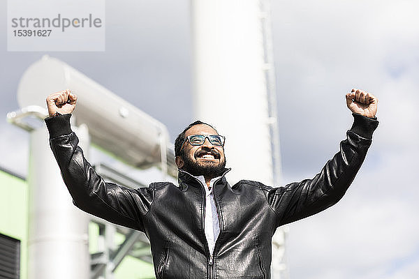 Porträt eines glücklichen Mannes mit Brille und schwarzer Lederjacke vor dem Kraftwerk