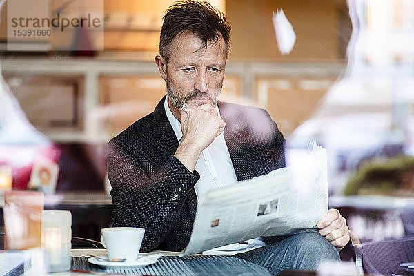 Porträt eines nachdenklichen reifen Geschäftsmannes  der in einem Café Zeitung liest