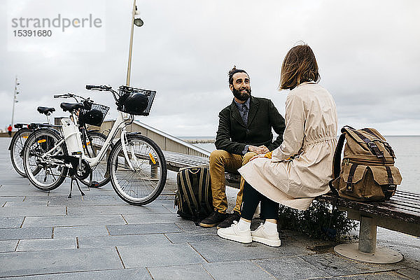 Ehepaar sitzt auf einer Bank an der Strandpromenade neben E-Bikes und unterhält sich